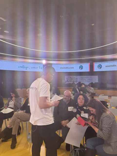 Un ponente reparte material entre el público durante un taller del II Encuentro ASEMDIS
