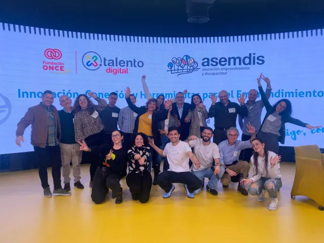 Foto de grupo de las personas asistentes al II Encuentro ASEMDIS ante la pantalla con los logotipos de Fundación ONCE, Por Talento Digital y ASEMDIS
