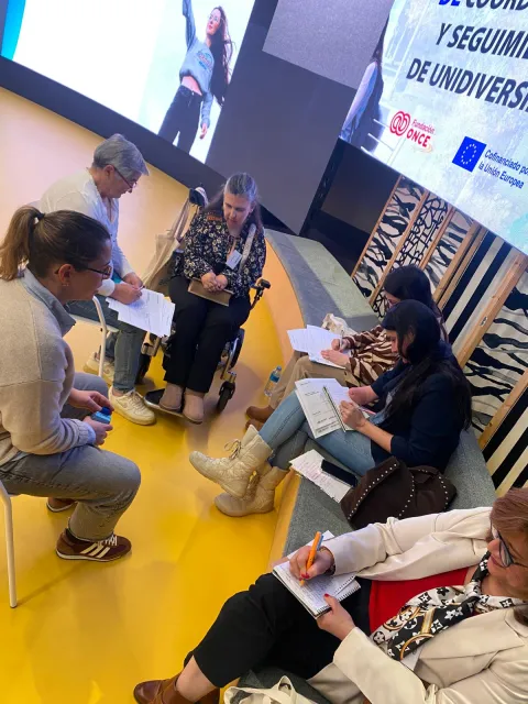Varias asistentes, una de ellas en silla de ruedas, toman notas sentadas en círculo durante un taller